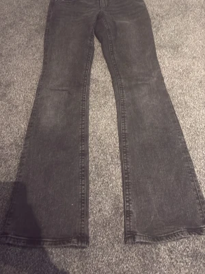 Svarta bootcut jeans från Pull&Bear - Säljer ett par svarta bootcut jeans från Pull&Bear med snygg tvättad look. Jeansen har framfickor med lock och silverfärgade knappar. Klassisk femficksmodell och bälteshällor. Perfekta för en trendig och avslappnad stil.