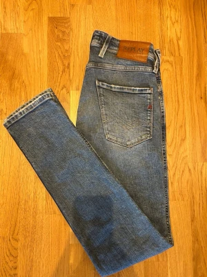 Blå raka jeans från Replay - Klassiska blå jeans från Replay med raka ben och femficksmodell. Jeansen har en snygg tvättad look, läderpatch med logga bak i midjan och diskreta slitningar. Perfekta för en avslappnad och trendig stil.