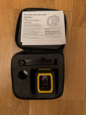 Mini Cross Line Laser Level i väska - Säljer en Mini Cross Line Laser Level i svart och gul plast med tillhörande skyddsväska och manual. Perfekt för att få raka linjer vid renovering eller inredning. Kompakt design och enkel att ta med sig. Drivs med AA-batterier (ingår ej).