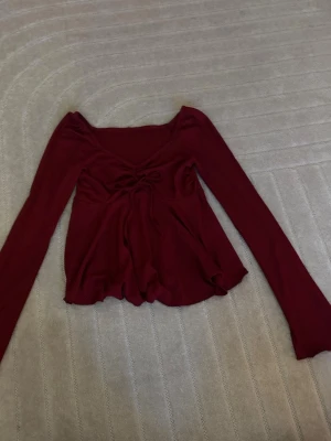 VinRöd långärmad topp med snörning - Trendig röd topp med långa ärmar och v-ringning. Toppen har snygg snörning framtill och är tillverkad i ett ribbat material som ger en skön och stretchig känsla. Perfekt för dig som vill ha en lite extra detalj på din outfit.