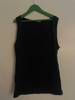 Svart linnetopp från Zara - En enkel och stilren svart linnetopp från Zara. Toppen är ärmlös med breda axelband och rund halsringning. Perfekt att matcha med jeans eller kjol för en clean look.