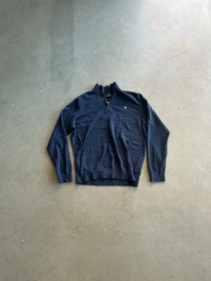 Morris quarterzip - Mörkblå stickad tröja med halv dragkedja och liten broderad logga på bröstet. Tröjan har ribbade muddar vid ärmslut och nederkant samt hög krage. Perfekt för lager på lager och en stilren look. Skriv vid frågor!