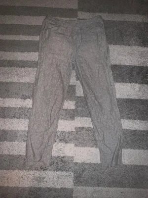 Grå linnebyxor med dragsko - Snygga grå linnebyxor med avslappnad passform och dragsko i midjan. Byxorna har raka ben och är tillverkade i ett svalt linnematerial som passar perfekt för varmare dagar. Enkla att matcha med både t-shirt och skjorta.