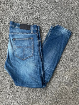 Blå tiger of sweden slim fit jeans med tvättade detaljer - Snygga blå slim fit jeans med tvättade detaljer och klassisk femficksdesign. Jeansen har normal midja, smala ben och kontrastsömmar. Tillverkade i denim med en cool sliten look som passar perfekt till en avslappnad stil.