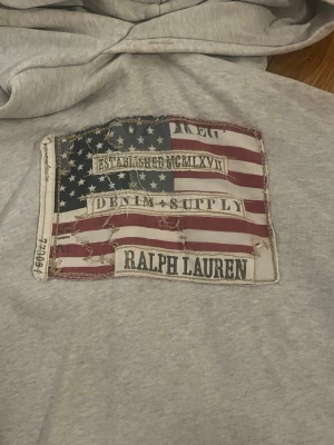 Grå hoodie från Ralph Lauren - Tunn snygg hoodie från Ralph Lauren! Ett litet hål precis vid fickan och en ljus fläck i slutet av armen, se bilder. Bara att skriva vid frågor!