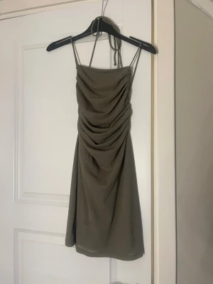 Grön kort klänning med snörning från Pull & Bear - Säljer en grön kort klänning med smala axelband och snygg drapering framtill. Klänningen har öppen rygg med snörning vilket gör passformen framtill justerbar. Den har dubbelt tyg vilket gör att man kan använda utan bh. Den sitter tajt men har ett stretchigt material som gör den bekväm ändå. Jag har klippt bort lappen i ryggen som kunde sticka fram. Perfekt till ett par klackar i sommar! Säljer eftersom jag växt ur den. Skriv vid frågor!🌸