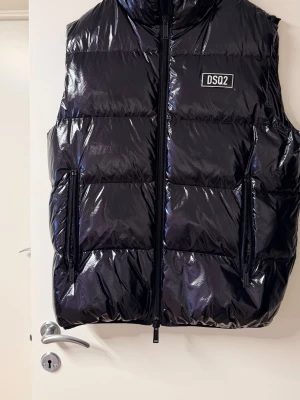 Dsquared Svart Pufferväst – Herr, Vinterjacka - Säljer en helt ny Dsquared2 puffer-väst i svart blank modell.  Aldrig använd.  Nypris ca 4 500 kr.  • Märke: Dsquared2 (DSQ2)  • Storlek: 54 (L/XL)  • Skick: NY  • Färg: svart  • Alla dragkedjor och detaljer perfekta   Trendigt designerplagg med exklusiv känsla och snygg passform.  Efterfrågad storlek.  Pris: 3 000kr Hjälp en 14 åring kunna köpa drömskor