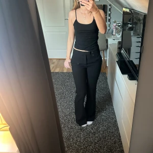 Svarta kostymbyxor med bootcut - Säljer ett par svarta kostymbyxor med bootcut-modell. Byxorna har två fuskfickor bak och stängs med dragkedja och hake fram. Snygg passform som ger en clean look.