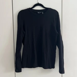 Svart långärmad topp - En enkel och stilren svart långärmad topp från Asos. Modellen har rund halsringning och är tillverkad i mjuk bomull som känns skön mot huden. Perfekt basplagg att matcha till olika outfits.