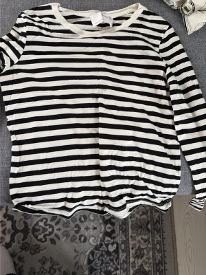 Randig långärmad tröja svart/vit - Säljer en långärmad tröja med svartvita horisontella ränder och rund halsringning. Tröjan har en avslappnad passform och är tillverkad i ett mjukt, tunt material som känns skönt mot huden. Perfekt för en enkel och stilren look.