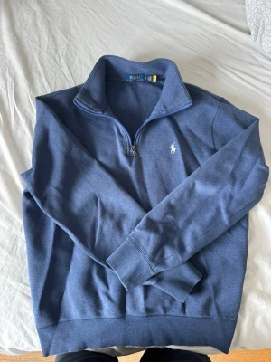 Blå M halvzip tröja från Polo Ralph Lauren  - Snygg blå stickad tröja från Polo Ralph Lauren med halv dragkedja och hög krage. Äkthetsbevis (QR-kodk) finns att skanna (se bilder) Tröjan har det klassiska vita logobroderiet på bröstet och ribbade muddar vid ärmslut och nederkant. Perfekt för lager på lager och stilren look. Den är lite nopprig längst nere men utöver det, riktigt bra skick. Medium i storlek. Nypris 2000