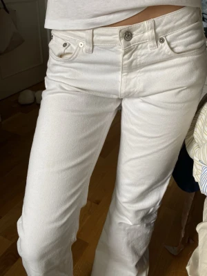 Vita bootcut jeans med låg midja - Säljer ett par vita jeans med utsvängda ben och låg midja. Jeansen har klassiska fem fickor, silverfärgade nitar och knapp, samt bälteshällor. Materialet är denim i bomull. Köpte från Sellpy och vill sälja vidare nu. 