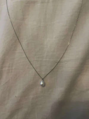 Silverhalsband med vit pärla - Ett stilrent halsband med tunn silverkedja och en droppformad vit pärla som hängsmycke. Rostfritt stål