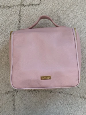 Rosa necessär från Don Donna - Snygg rosa necessär från Don Donna med guldfärgade detaljer och flera fack för smart förvaring. Tillverkad i ett mjukt material med praktiskt handtag upptill och dragkedja runt om. Perfekt för att organisera smink eller hygienprodukter.