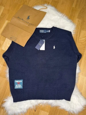 Mörkblå stickad tröja Polo Ralph Lauren Stl. S - Oanvönd mörkblå stickad Polo Ralp Luren tröja med design på baksidan. Tröjan är egentligen Dam i stl. S men enligt mig passar ddn också Herr i XS. Påsen ingår!