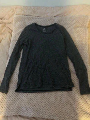 Mörkgrå långärmad topp H&M Basic - En enkel och stilren mörkgrå långärmad tröja från H&M. Tröjan har rund halsringning och normal passform. Perfekt att matcha med jeans eller kjol för en clean look.