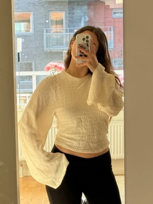 Vit croppad topp med vida ärmar - Säljer en vit croppad topp med vida sjukt fina långärmar och strukturmönster. Toppens material känns mjukt och har en tunn och lätt textur. Använd 1 gång till en middag. Säljer för att den helt enkelt blivit för stor för mig. Toppen är från Gina tricot, originalpris 359,95kr