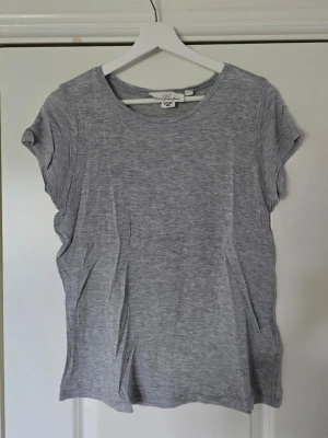 Grå basic t-shirt från H&M - En enkel och stilren grå t-shirt från H&M i mjukt och tunt material. T-shirten har rund halsringning och korta ärmar. Tillverkad i 100% lyocell vilket gör den extra skön och luftig. Perfekt till alla dina outfits.