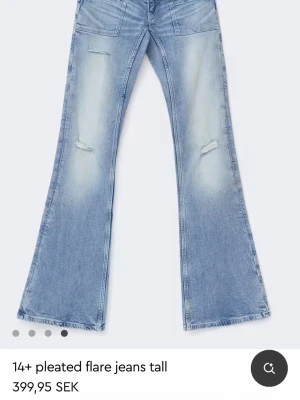 Ljusblå utsvängda jeans med slitningar - Säljer ett par ljusblå flare jeans med låg midja och slitna detaljer på låren. Jeansen har vida ben och klassiska fickor både fram och bak.