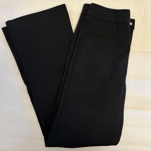 Svarta klassiska kostymbyxor från Zara  - Svarta kostymbyxor som är i kortare modell med utsvängda ben nertill från Zara i storlek XS. Byxorna har två stilrena fickor framtill, dragkedja samt knäppning. 