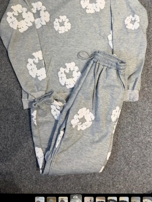 Grått loungewear-set med blommor - Mysigt loungewear-set i ljusgrått med vita blommönster. Setet består av en sweatshirt med långa ärmar och matchande byxor med resår i midjan och benslut. Perfekt för chill dagar hemma. Mjukt material som känns skönt mot huden.