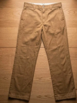 Slim fit chinos från Dickies - Snygga bruna slim fit chinos från Dickies med klassisk design och raka ben. Byxorna har hällor för bälte, knappstängning och är tillverkade i ett slitstarkt bomullsmaterial. Perfekta för dig som vill ha en stilren och bekväm look.