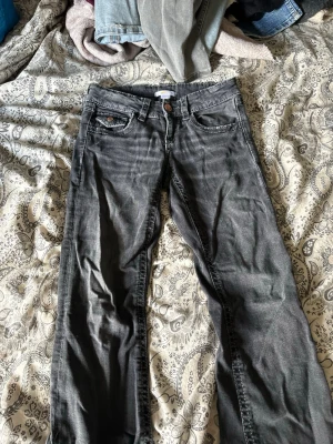 Mörkgrå raka jeans med knappar - Säljer ett par mörkgrå jeans med raka ben och klassisk femficksmodell. Jeansen har snygga kontrastsömmar och detaljerade bakfickor med knappar. Perfekta för en avslappnad och cool stil.