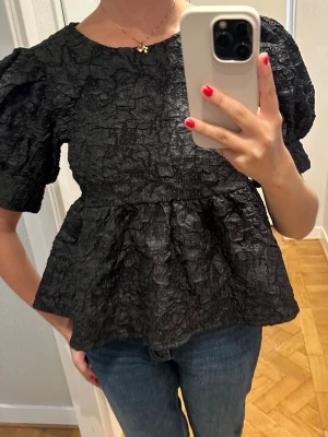 Svart topp med puffärm och struktur - Säljer en svart topp med puffärmar och rund hals. Toppen har en unik, skrynklig struktur i materialet och en lätt utsvängd passform nedtill. Från Vero Moda, använd en gång.
