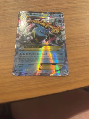 Pokémonkort M Blastoise EX holo - Säljer ett Pokémonkort av modellen M Blastoise EX med holografisk yta. Kortet har färger i blått, silver och regnbågsskimrande detaljer. Perfekt för samlare eller dig som vill uppgradera din kortlek med en riktigt cool och sällsynt Blastoise.