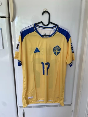 Svensk landslagströja Adidas gul/blå - Säljer en officiell svensk landslagströja från Adidas i gul med blå detaljer. Tröjan har nummer 17 och 11 på framsidan, broderad landslagssköld och Adidas-logga. Tillverkad i lätt och ventilerande funktionsmaterial, perfekt för fotboll eller träning.