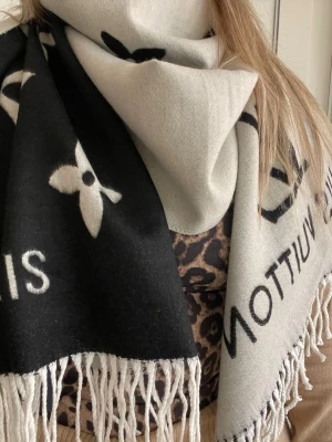 Svartvit  Vuitton halsduk - Säljer en svartvit halsduk från  Vuitton med ikoniska monogram och texten PARIS. Halsduken har långa fransar i ändarna och är tillverkad i ett mjukt material som känns lyxigt. Perfekt accessoar för att lyfta din outfit.