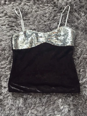 Svart och silver paljettopp - Snygg topp med svarta sammetsdetaljer och glittrig silverpaljett upptill. Axelbandsmodell med smala band och croppad passform. Perfekt för dig som vill sticka ut med lite extra bling.
