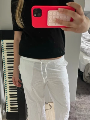 Vita linnebyxor med dragsko - Säljer ett par vita linnebyxor med avslappnad passform och dragsko i midjan. Byxorna har raka ben och resår i midjan för extra komfort. Perfekta för en chill och stilren look. Materialet är lätt och luftigt linne.