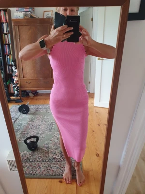 Rosa ribbad midiklänning - Säljer en snygg rosa ribbad midiklänning med ärmlös design och rund hals. Klänningen har en tight passform och slits på sidan för extra stilpoäng. Perfekt för dig som gillar färg och vill sticka ut lite extra.