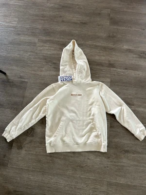 Vit hoodie från Jack & Jones - Snygg vit hoodie från Jack & Jones med broderad text 'Originals Club' på bröstet. Klassisk känguruficka framtill och stor huva. Tillverkad i mjuk bomullsmix som känns skön mot huden. Perfekt för en avslappnad och trendig look.