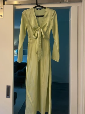 Ljusgrön långklänning Gina Tricot - Snygg ljusgrön långklänning från Gina Tricot i ett glansigt material. Klänningen har v-ringning, lång ärm och en knyt-detalj framtill som ger en feminin touch. Perfekt för dig som vill sticka ut med en stilren look.