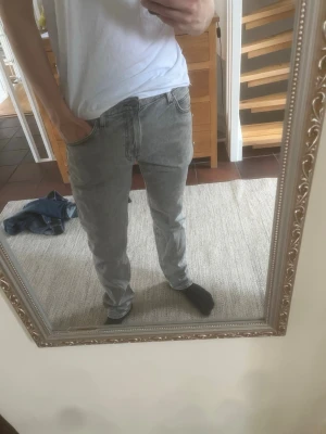 Grå slim fit jeans från Lee - Säljer ett par grå slim fit jeans från Lee med klassisk femficksdesign och dragkedjegylf. Jeansen har en snygg tvättad look och raka ben. Perfekta för dig som gillar en stilren och avslappnad vibe.