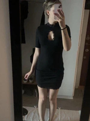 Svart kort spetsklänning - Säljer en svart kort klänning med spetsdetaljer vid halsringningen och nederkanten. Klänningen har en snygg öppning vid bröstet och korta ärmar. Sitter tight och har en elegant, feminin look. Den är helt ny från shein och helt oanvänd den har super mjukt material också