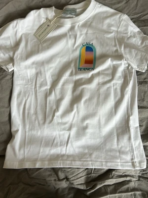 Vit Casa Blanca t-shirt med tryck - Säljer en vit t-shirt från Casa Blanca med färgglatt grafiskt tryck fram och stort tryck på ryggen. T-shirten har rund hals och korta ärmar. Materialet är mjuk bomull och passformen är normal. Perfekt för dig som gillar stilrena plagg med unik design.