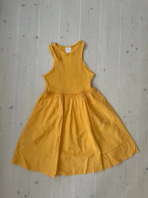 Gul ribbad sommarklänning från Zara - Snygg gul klänning från Zara med ribbad överdel och rund halsringning. Kjoldelen är i mjuk bomull och har en lätt utställd form. Perfekt för varma dagar och ger en fräsch look.
