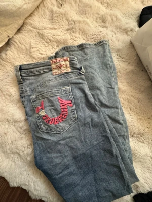 True Religion ljusblå jeans med brodyr - Säljer ett par ljusblå jeans från True Religion med ikonisk rosa brodyr. Jätte fint skick och inga problem. 💕Tvecka inte på att skriva vid frågor och pris går alltid att diskutera.🤗