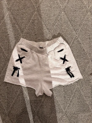 Vita shorts med svarta snördetaljer - Snygga vita shorts med elastisk midja och svarta snördetaljer framtill. Perfekta för varma dagar och en avslappnad stil.