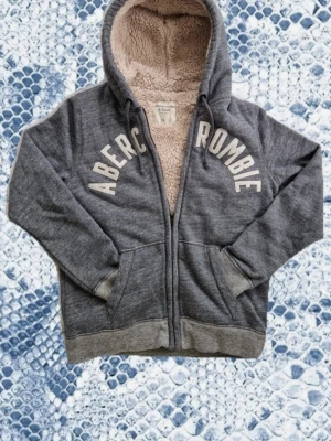 Abercrombie & Fitch hoodie grå fodrad - Abercrombie & Fitch hoodie i extremt fint skick. Storlek S/M. Hoodien har en varm päls som gör den fodrad, passar perfekt till milda sommarkvällar.  Mått: Armlängd: 66cm armhåla-armhåla (bredd) : 52cm Armbredd: 15cm axel-midjeslut (längd) : 63cm