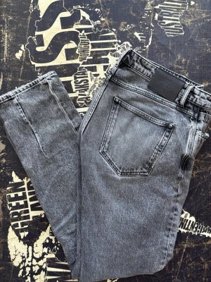 Grå tvättade raka jeans från neuw  - Säljer ett par grå tvättade jeans med rak passform och klassiska bakfickor. Jeansen har en svart patch vid linningen och är tillverkade i ett slitstarkt denimtyg. Perfekta för en avslappnad och trendig look.