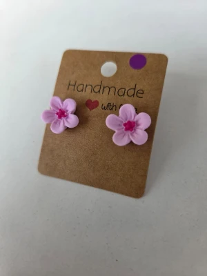 Handgjorda rosa blomörhängen - Supersöta handgjorda örhängen i form av ljusrosa blommor med mörkare rosa detaljer i mitten. Örhängena är små och diskreta, men ger ändå en färgklick. Stiften är av rostfritt stål. Örhängena är gjorda för hand av mig i polymerlera.