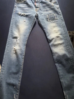 Ljusblå slitna jeans med patch - Säljer ett par ljusblå dsquared  jeans med slitningar och patchdetalj på ena låret. Jeansen har raka ben och klassisk femficksmodell. Perfekta för en avslappnad och trendig look. Passar folk i xs s och m