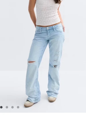 Ljusblå loose bootcut jeans - Säljer ett par ljusblå bootcut jeans med slitningar på båda benen och klassisk femficksdesign. Jeansen har låg midja och vida ben. Köpta på Vinted.