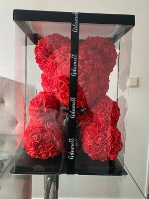 Nallebjörn av röda rosor i presentbox - Unik nallebjörn gjord av konstgjorda röda rosor, levereras i en genomskinlig presentbox med svart band. Perfekt som dekor eller gåva till någon speciell. Nallen har en klassisk björnform och är täckt av tätt placerade rosor.