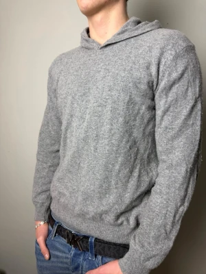 Grå hoodie i kashmir från Oscar Jaconson - Mjuk och stilren grå hoodie från Oscar Jacobson.                                                                   Storleken på tröjan är xl men den har krympt i tvätten till m. Modellen har vanligtvis m.                Skicket är som nytt endast mindre i storlek 