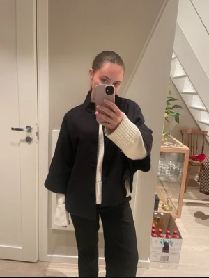 Svart kort jacka med knappar - Stilren svart jacka med rak passform och knäppning framtill. Jackan har en hög krage och vida, något kortare ärmar. Perfekt för lager-på-lager och enkel att matcha med olika outfits.